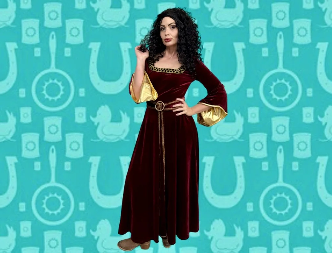 A woman with curly black hair wearing a long, dark red velvet dress with gold accents and wide gold sleeves, standing in front of a teal background with horse and money patterns.