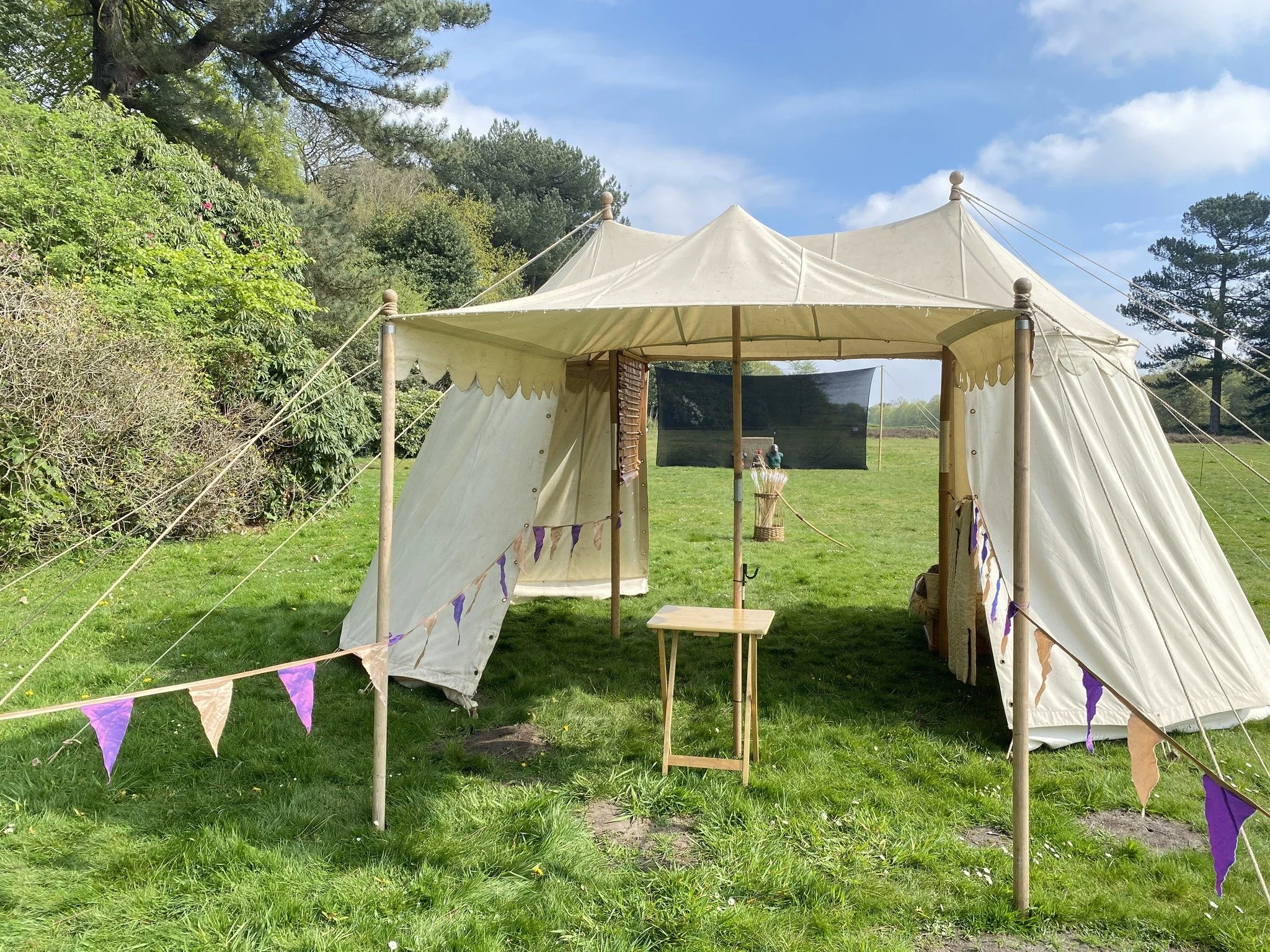 White medieval style tent in a formal garden with a have-a-go archery range behind