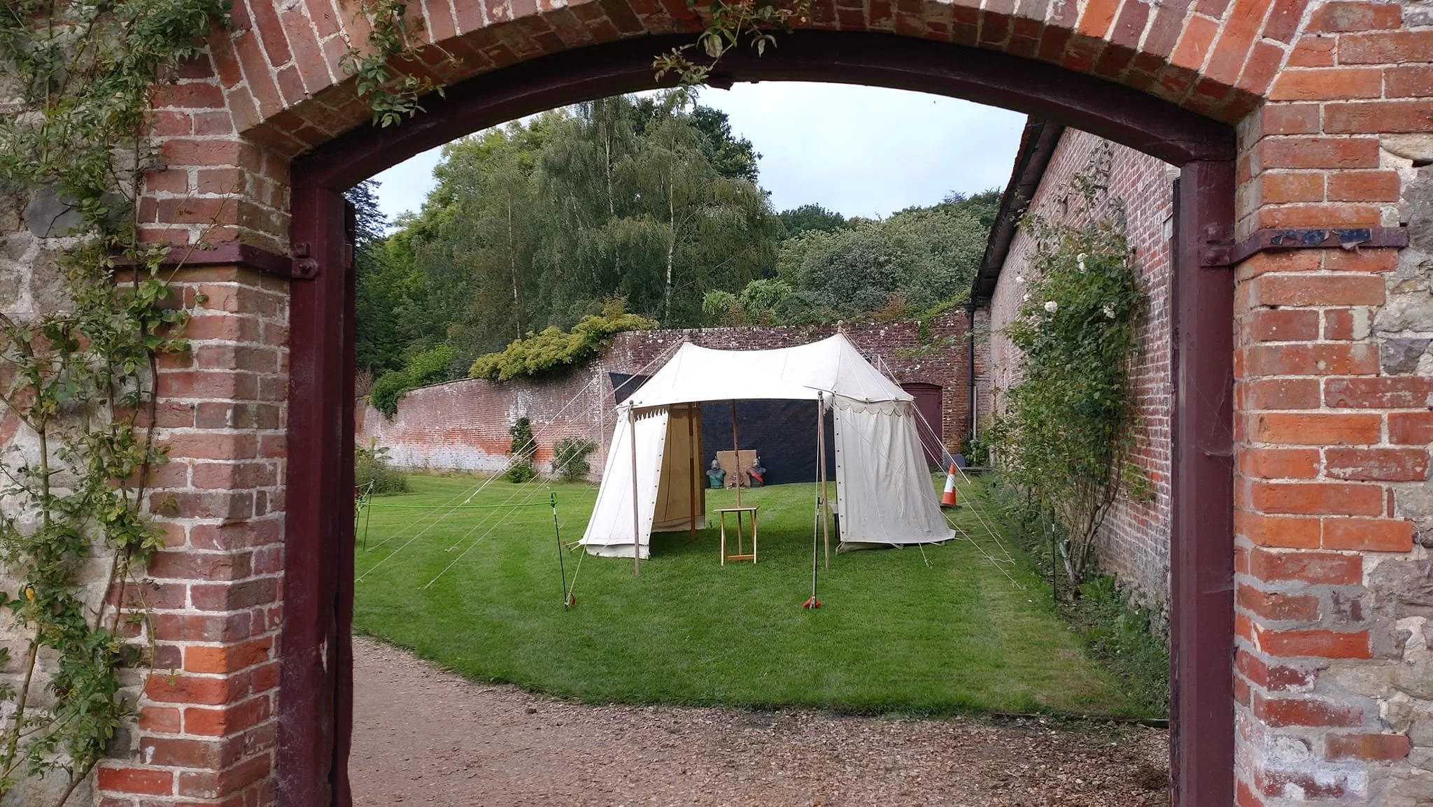 Glimpse of white tent and archery range through an old brick archway at a formal garden