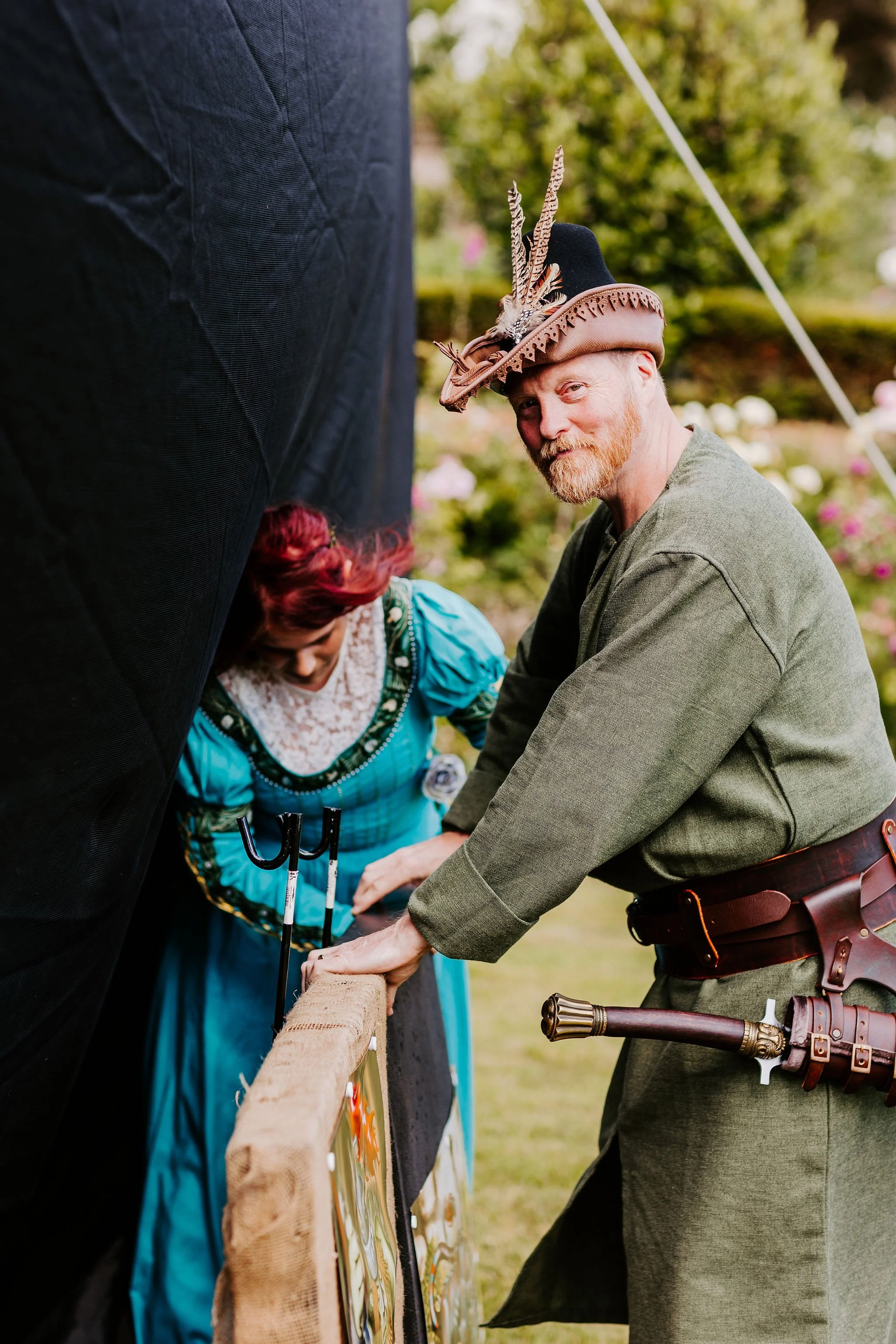 Smiling groom with sword on his belt and wedding guest in long dress inspecting arrows in archery target