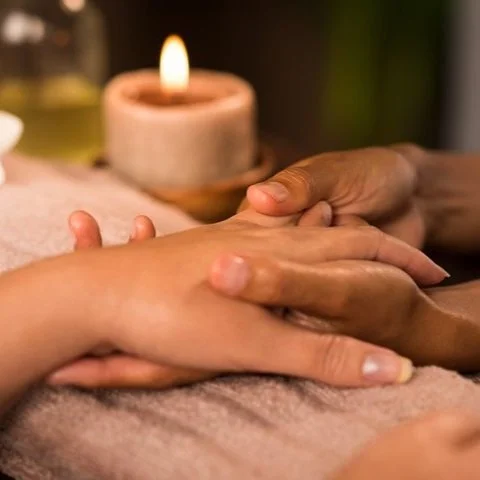 Close-up of a person receiving a hand massage with a lit candle in the background.
