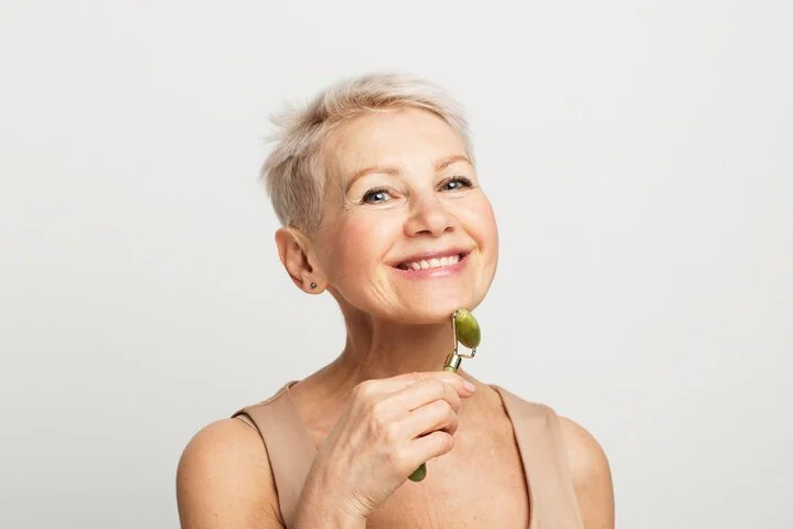 Mujer mayor con cabello rubio corto, sonriendo y usando un esmalte de uñas verde, con un fondo blanco