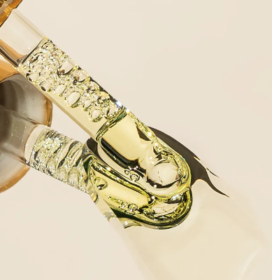 Ampolla con líquido transparente, viscoso y brillante, que gotea sobre una superficie clara.