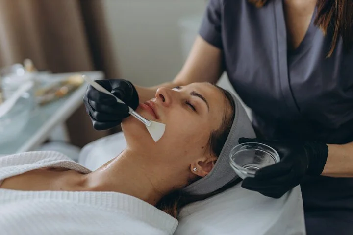Procedimiento de limpieza facial en un rostro de mujer con un profesional usando guantes negros, aplicando un instrumento en la boca de la paciente que está acostada en una camilla