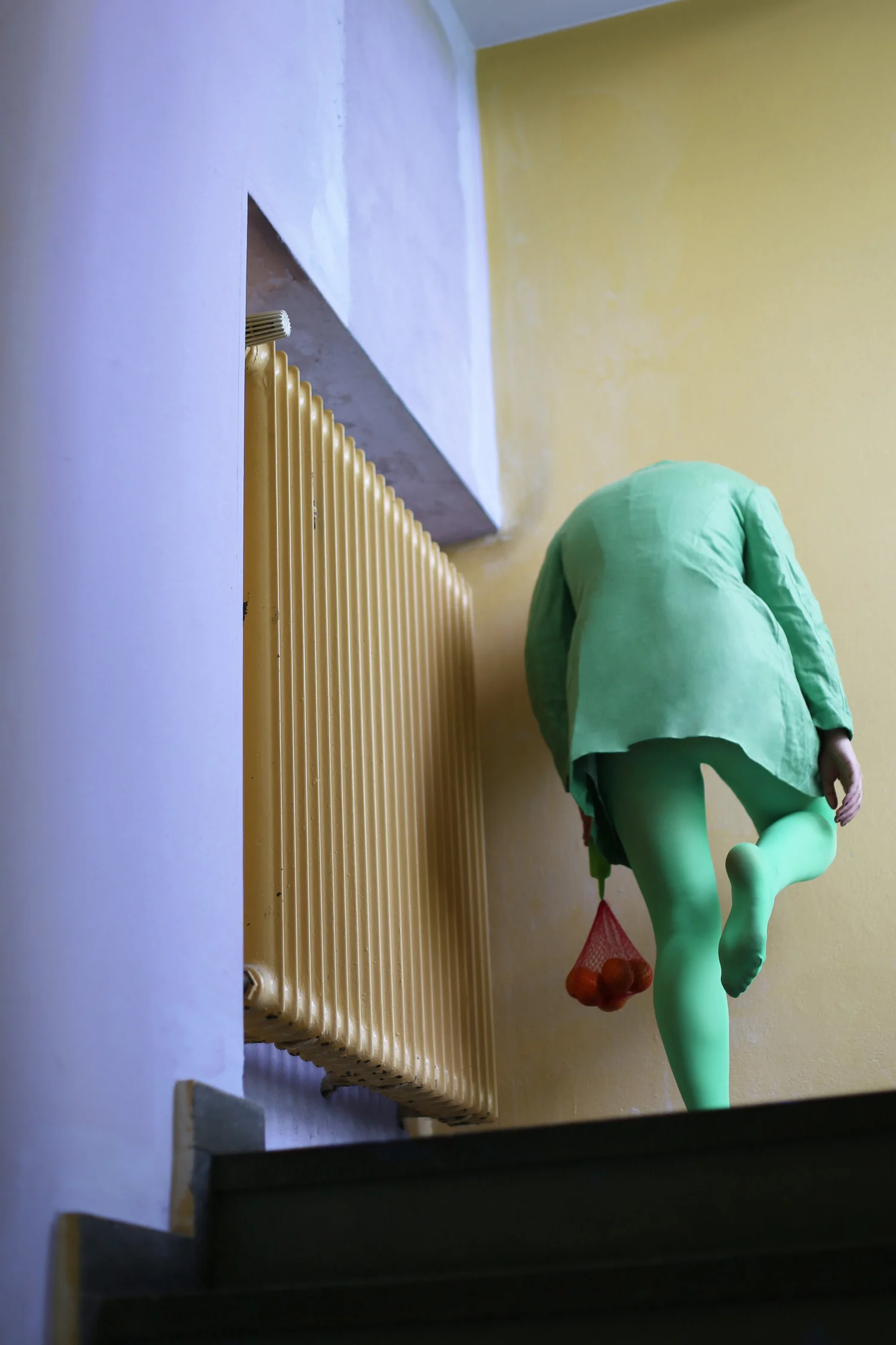 A person in a green outfit carrying a red net bag, climbing yellow stairs