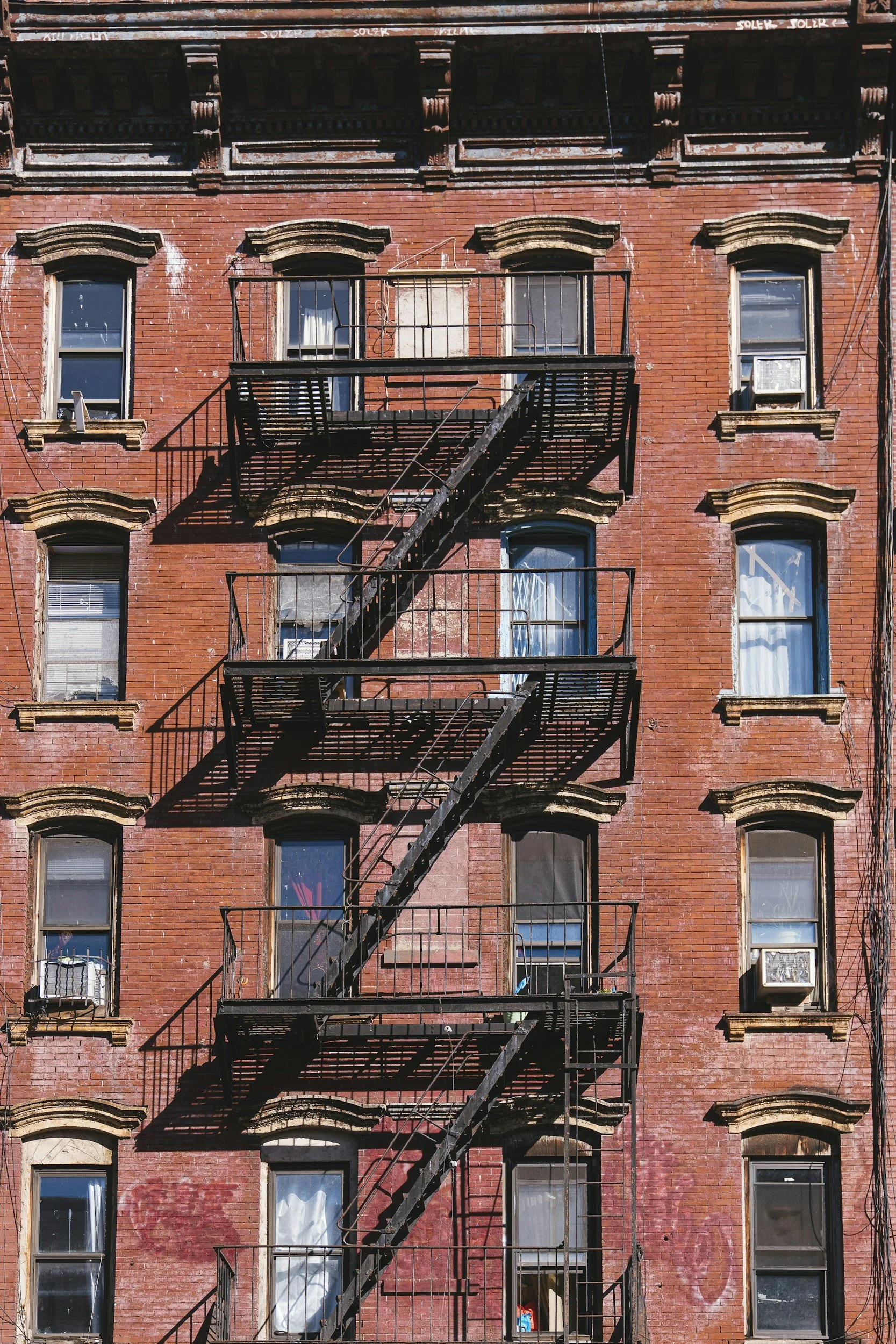 Brick apartment building with fire escape stairs and multiple windows, some with air conditioning units.