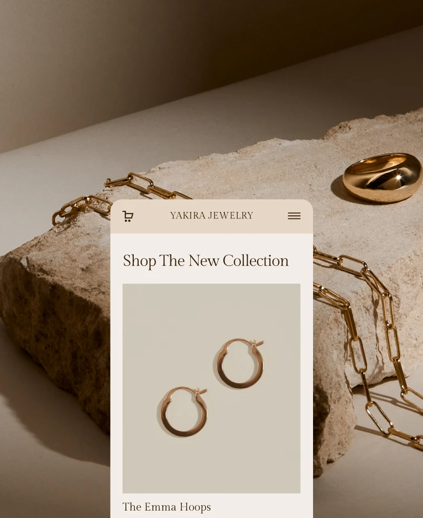 An online jewelry store storefront for Yakira Jewelry displaying hoop earrings called The Emma Hoops, with a gold chain and ring placed on a stone surface.
