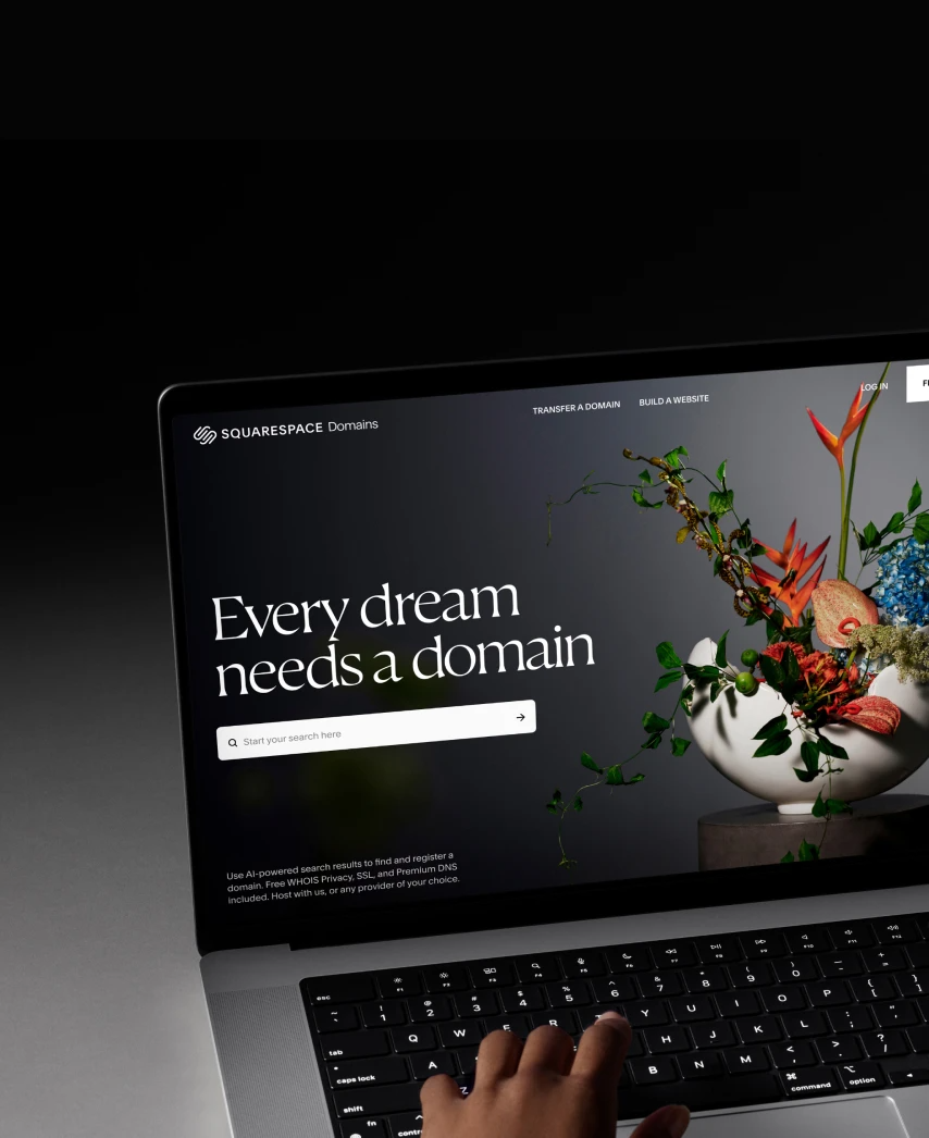 A person using a laptop displays the Squarespace website with the slogan "Every dream needs a domain" and a floral arrangement on the screen.
