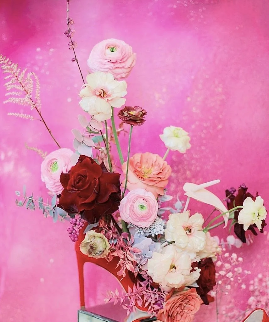 A floral arrangement inside a high-heeled shoe with pink background.