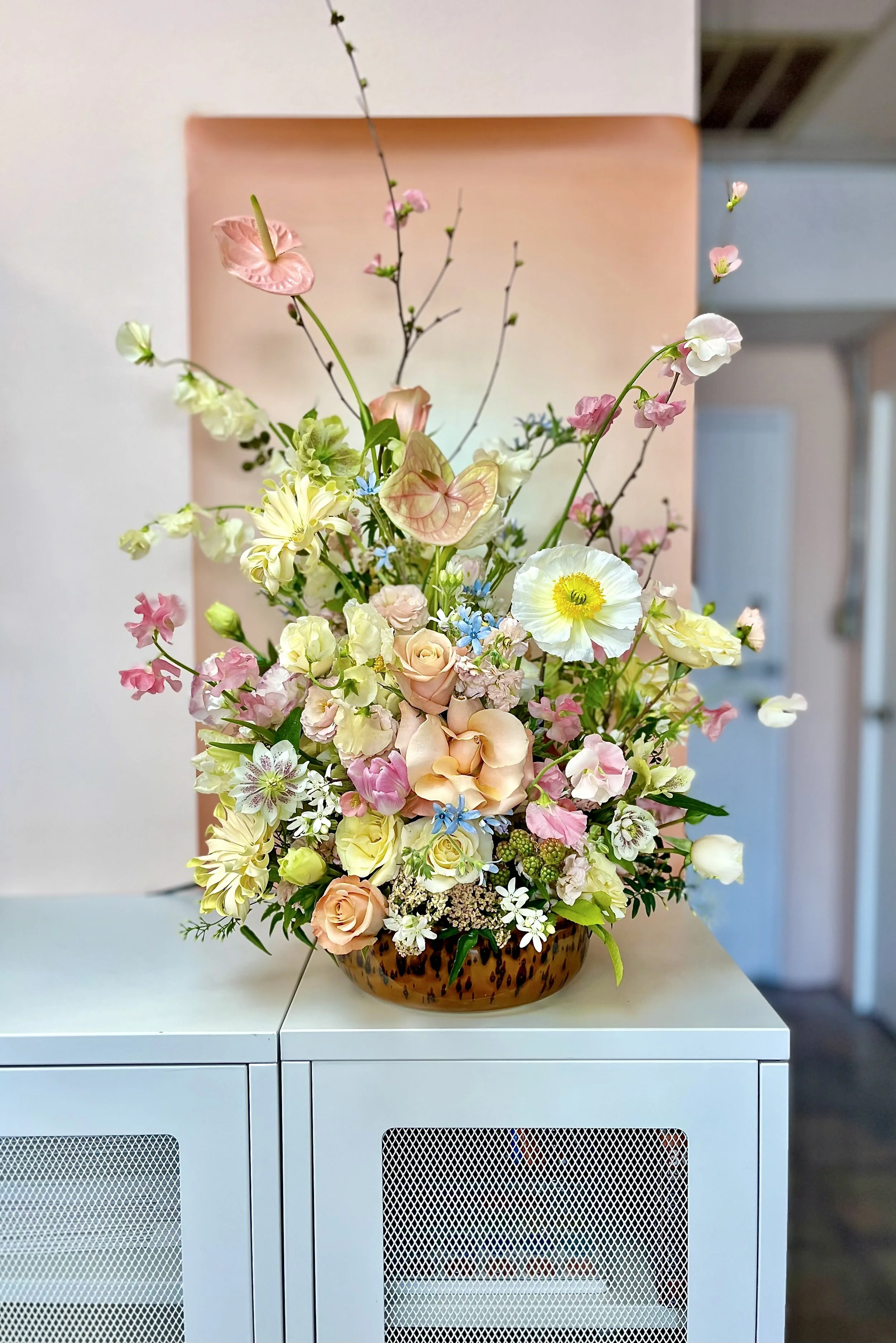 An arrangement of mixed flowers in a brown, leopard-print bowl on a white cabinet.