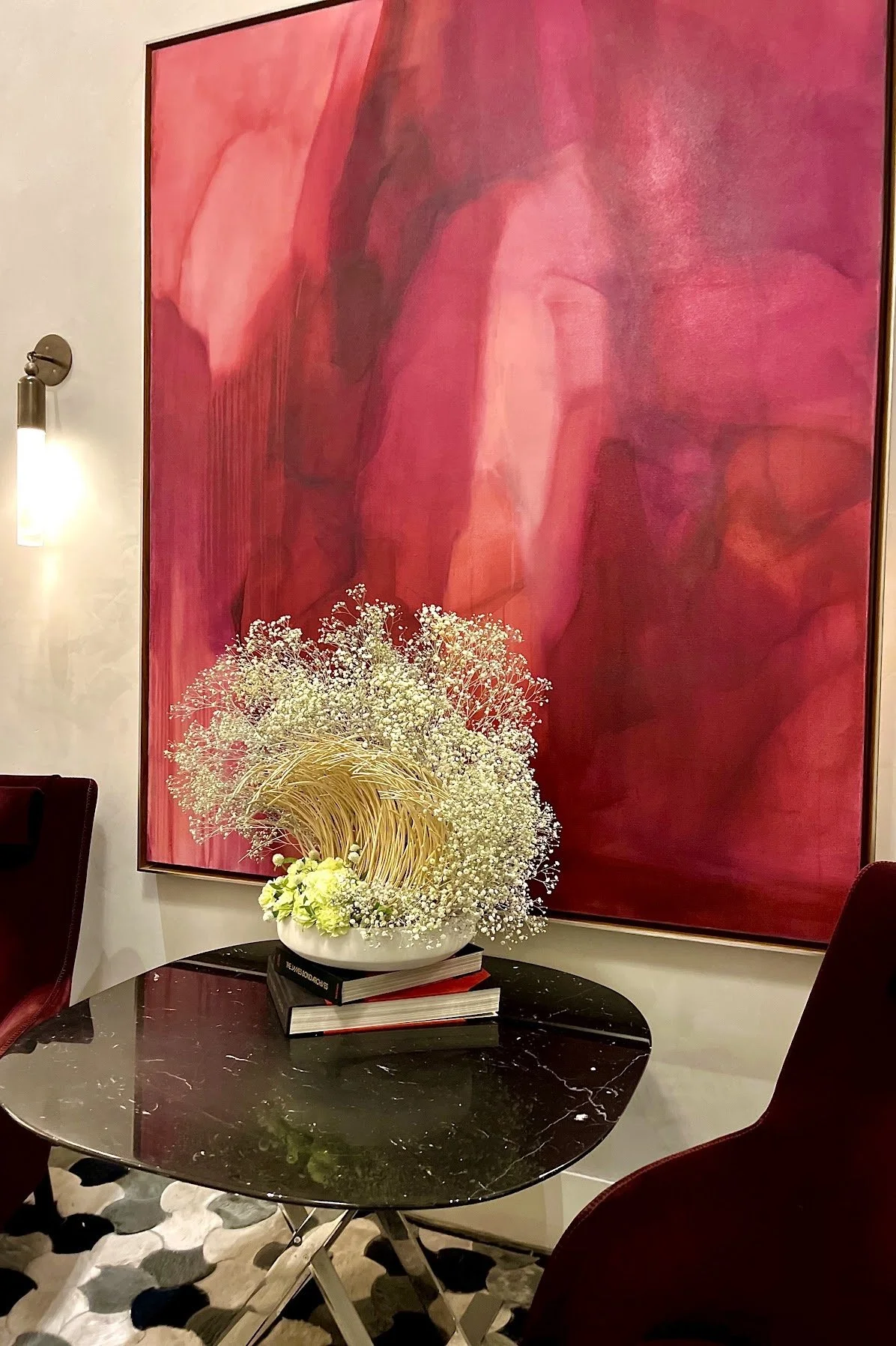 Decorative floral arrangement on a black marble table with modern chairs in a room featuring a large abstract pink and red painting on the wall.