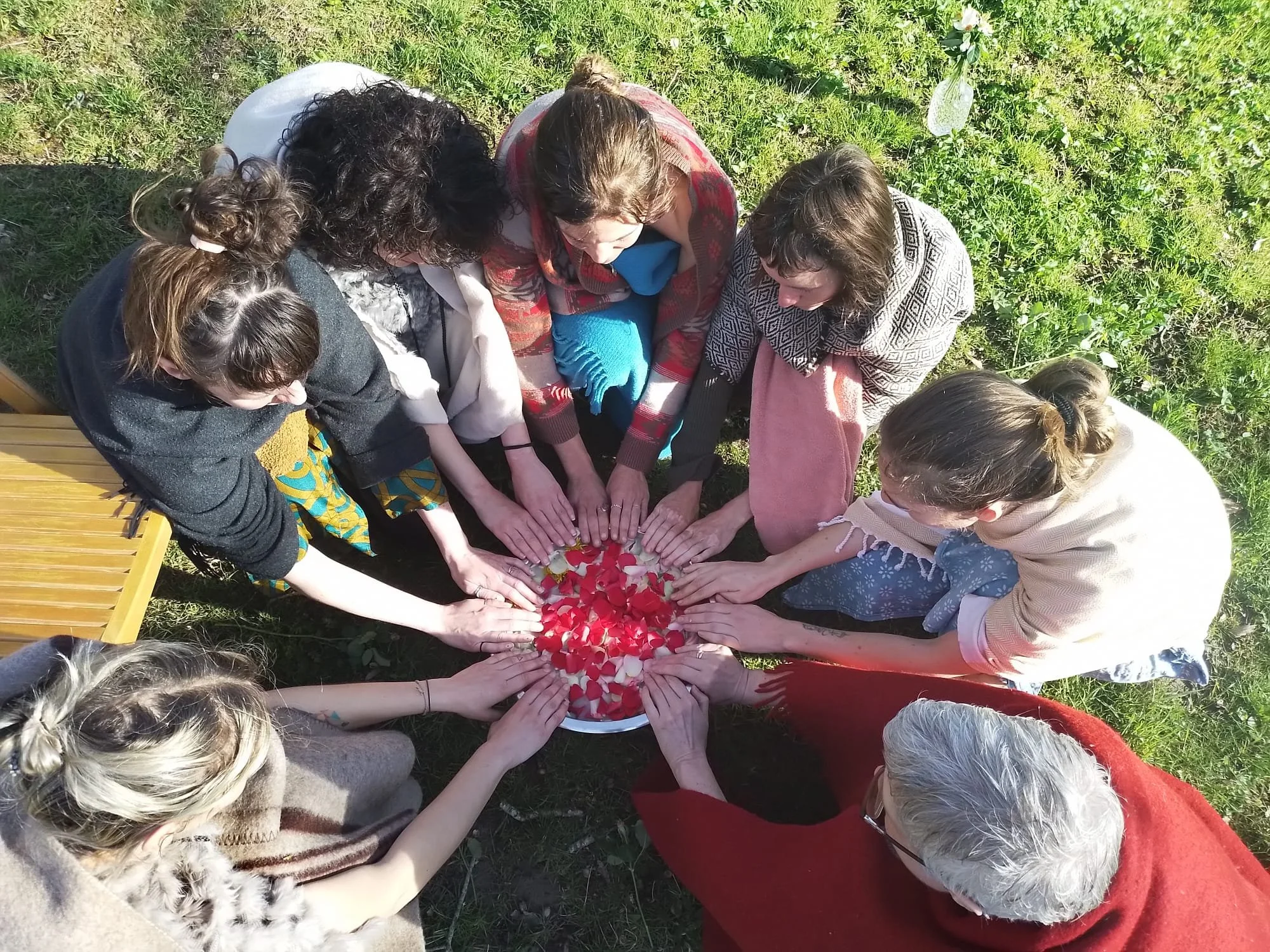 Group of women gathered in a circle outdoors with their hands together over a tray of flower petals.