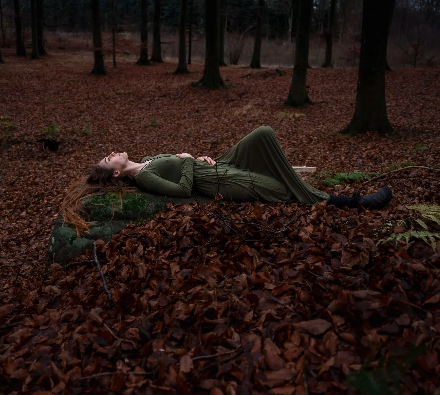 Kaya in a green dress lying on a rock in a Beech forest with fallen leaves.
