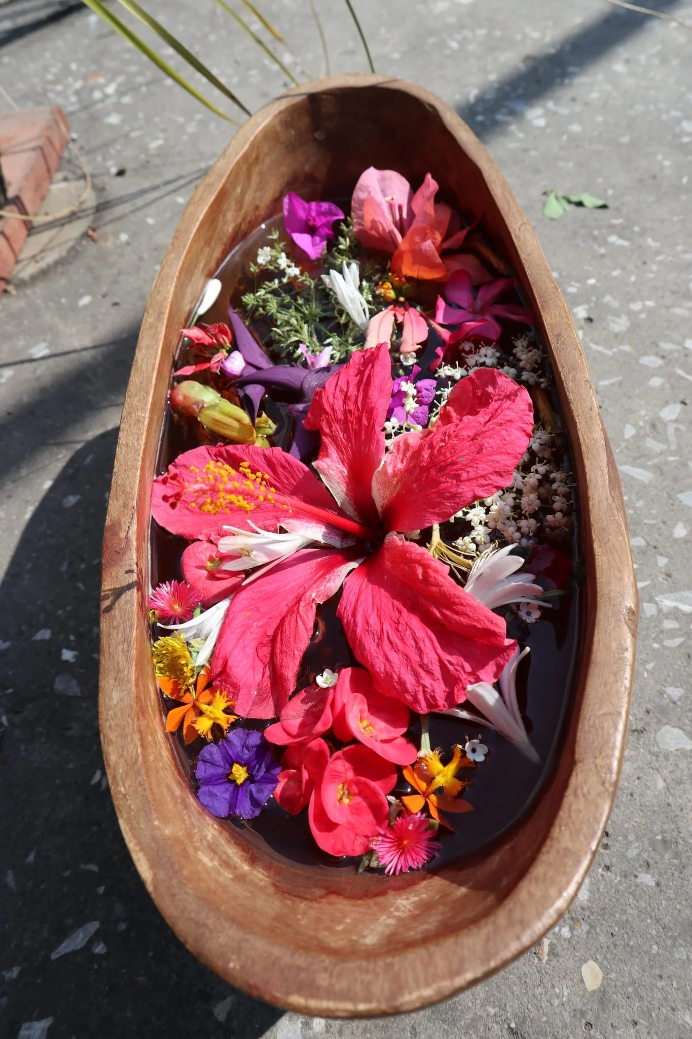 A wooden bowl filled with water and various colorful flowers floating on top.