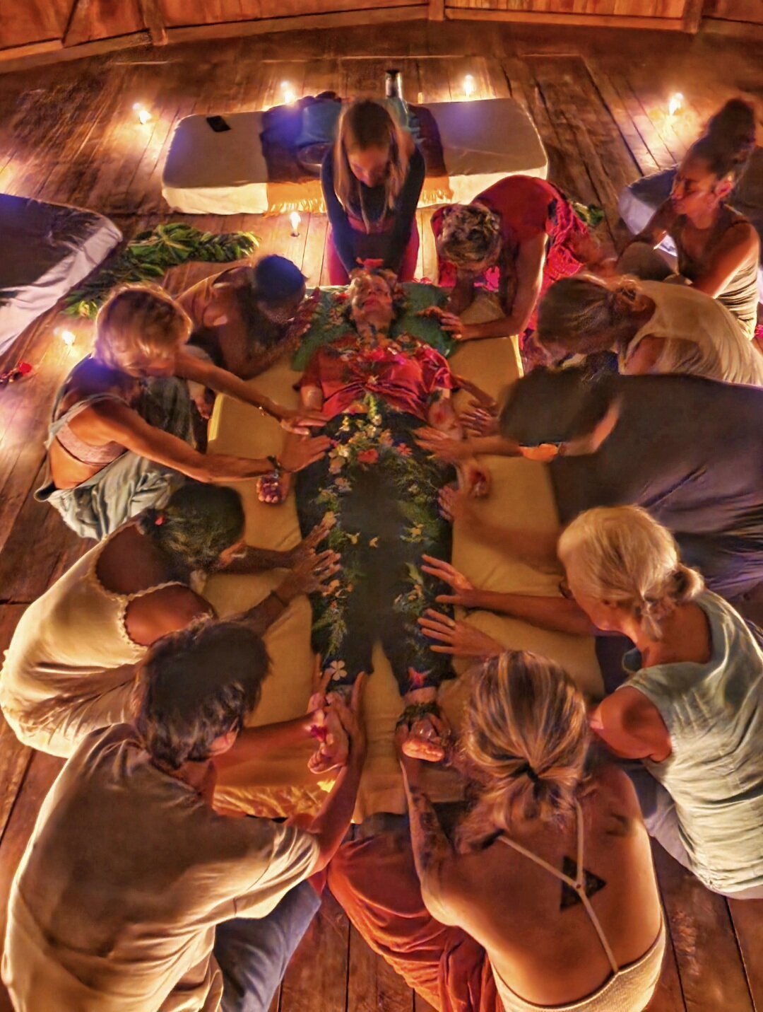 A group of women gathered around a person lying on a table in a ritualistic setting with candles around them, performing a womb healing ritual.