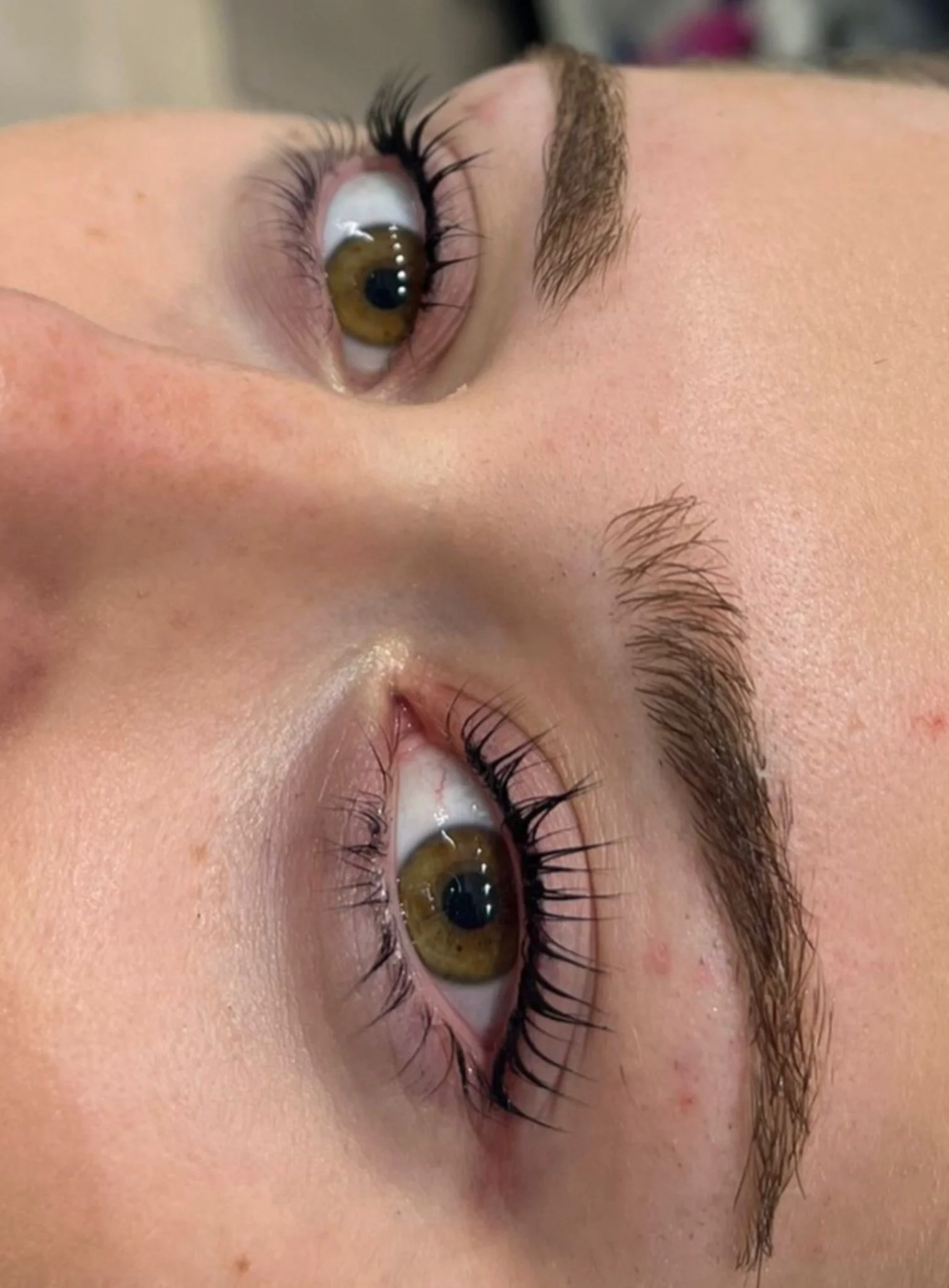 Close-up of a person's face with brown eyes, long eyelashes, and well-groomed eyebrows, lying on their side.