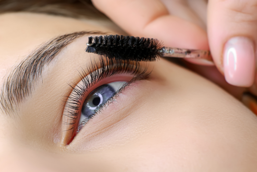 Close-up of a person eyelash being coated with mascara using a wand.