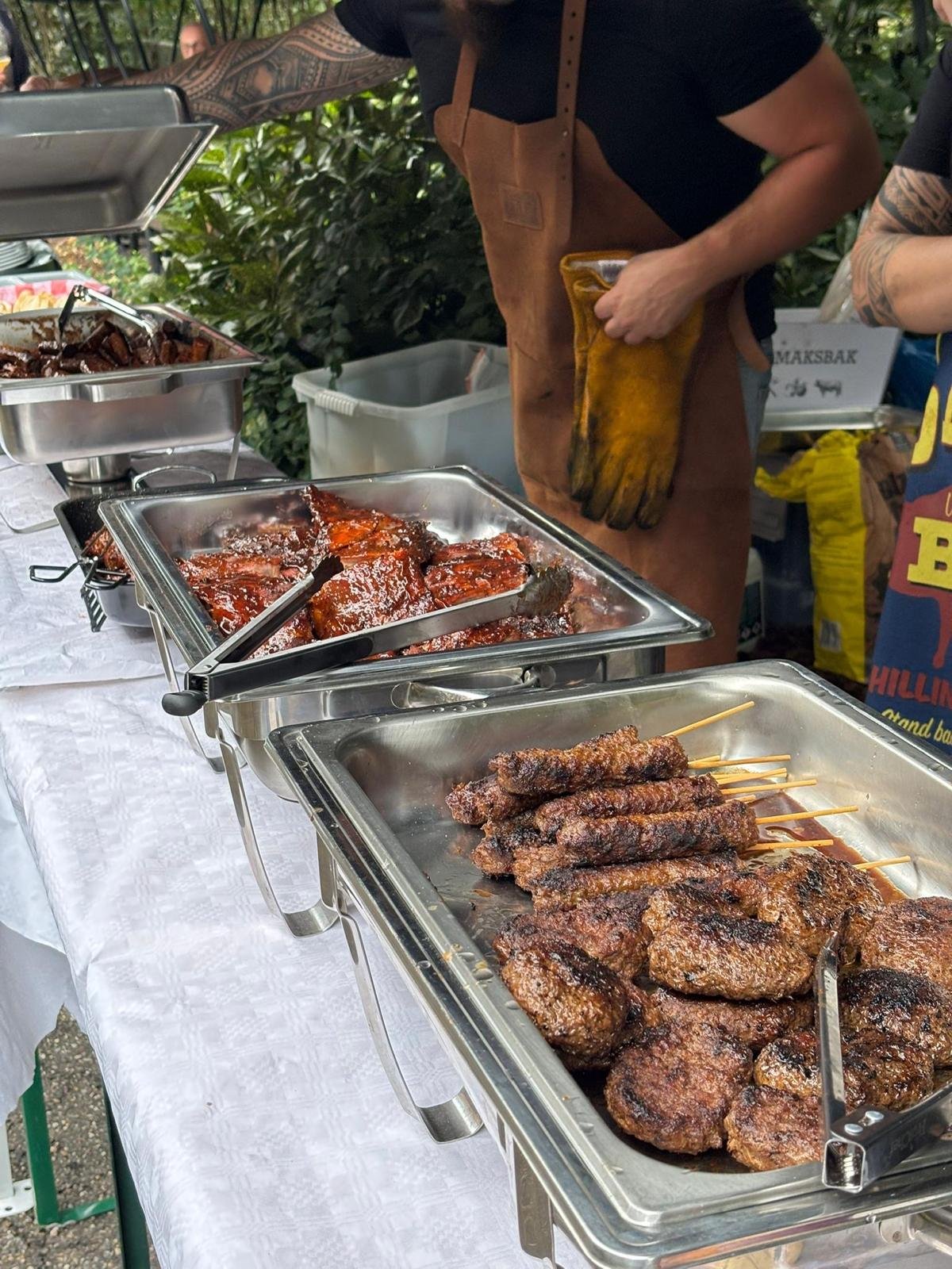Buffet met gemarineerde en gegrilde vleeswaren, waaronder hamburgers en spiesjes, op een feest of markt.