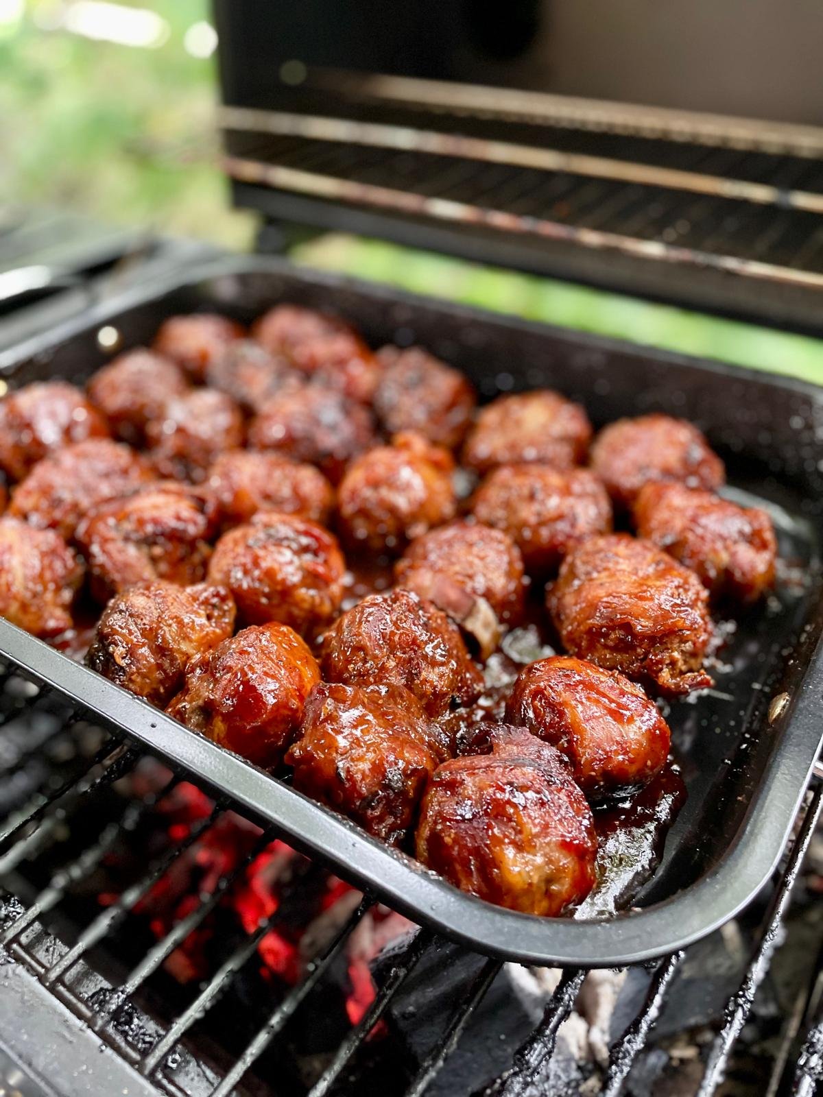 Worstelende kippenballetjes in barbecuesaus op een grillplaat buiten.