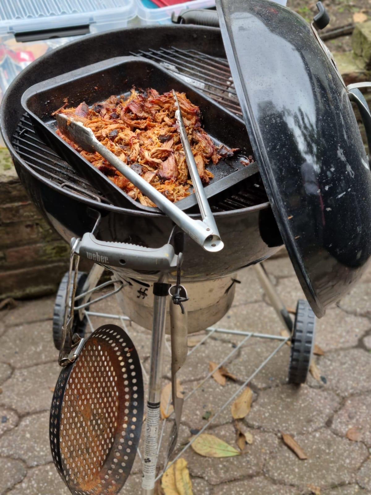Gekraakte en uit elkaar vallende geroosterde stukjes vlees op een barbecue met een deksel open.