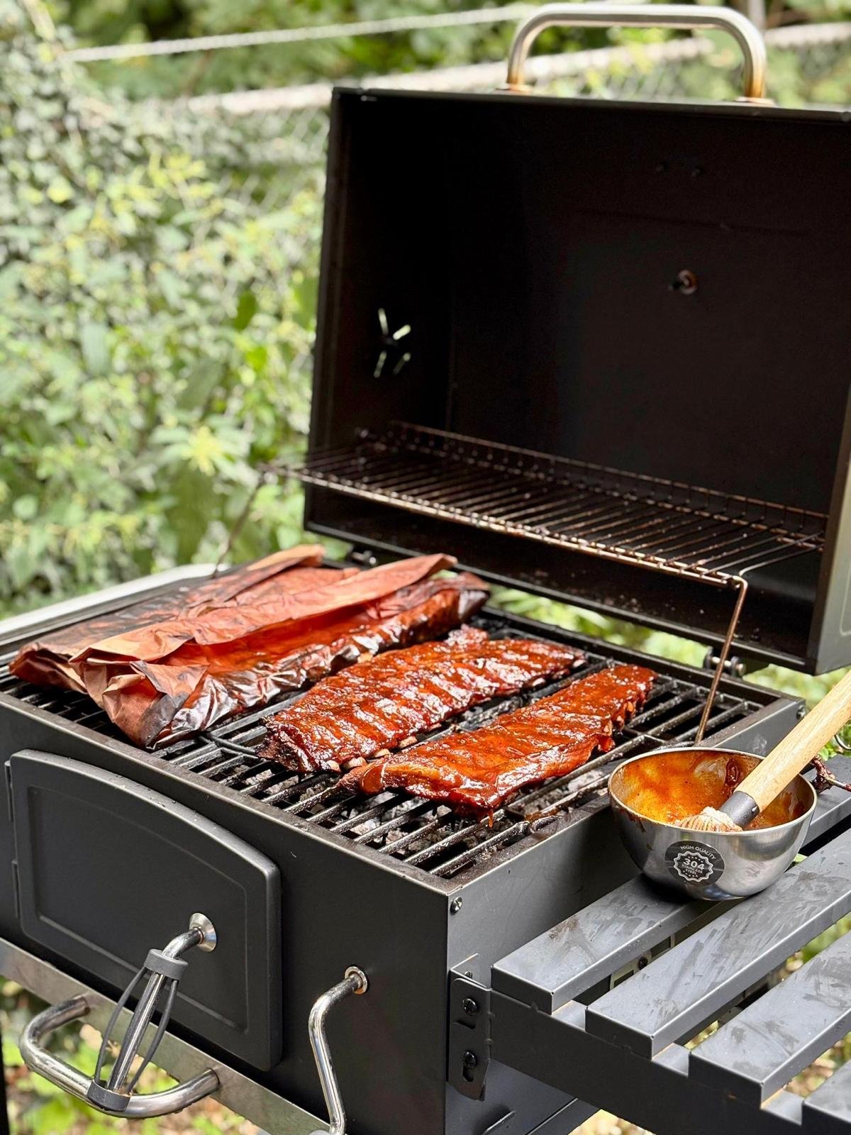 Barbecue grill met ribs en een bak met saus, buiten in een tuin