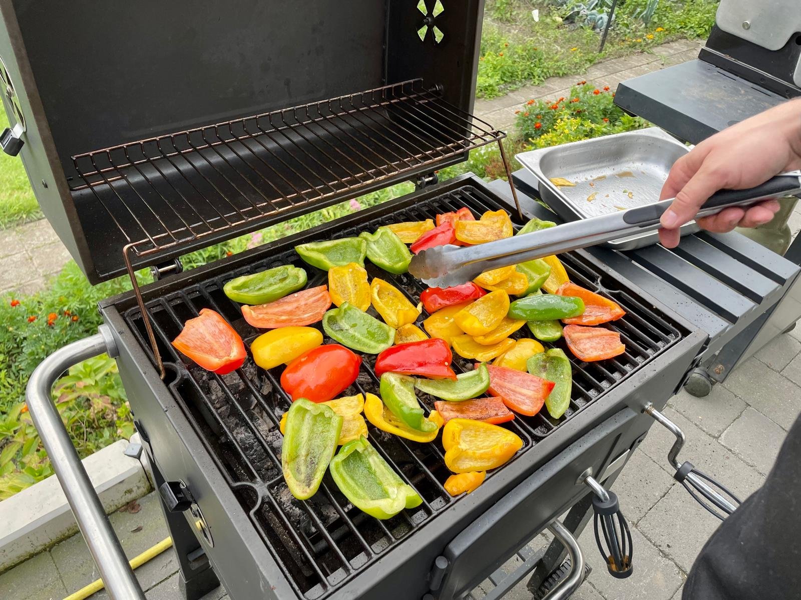 Groene, gele, rode en oranje paprika's worden gegrild op een barbecue.