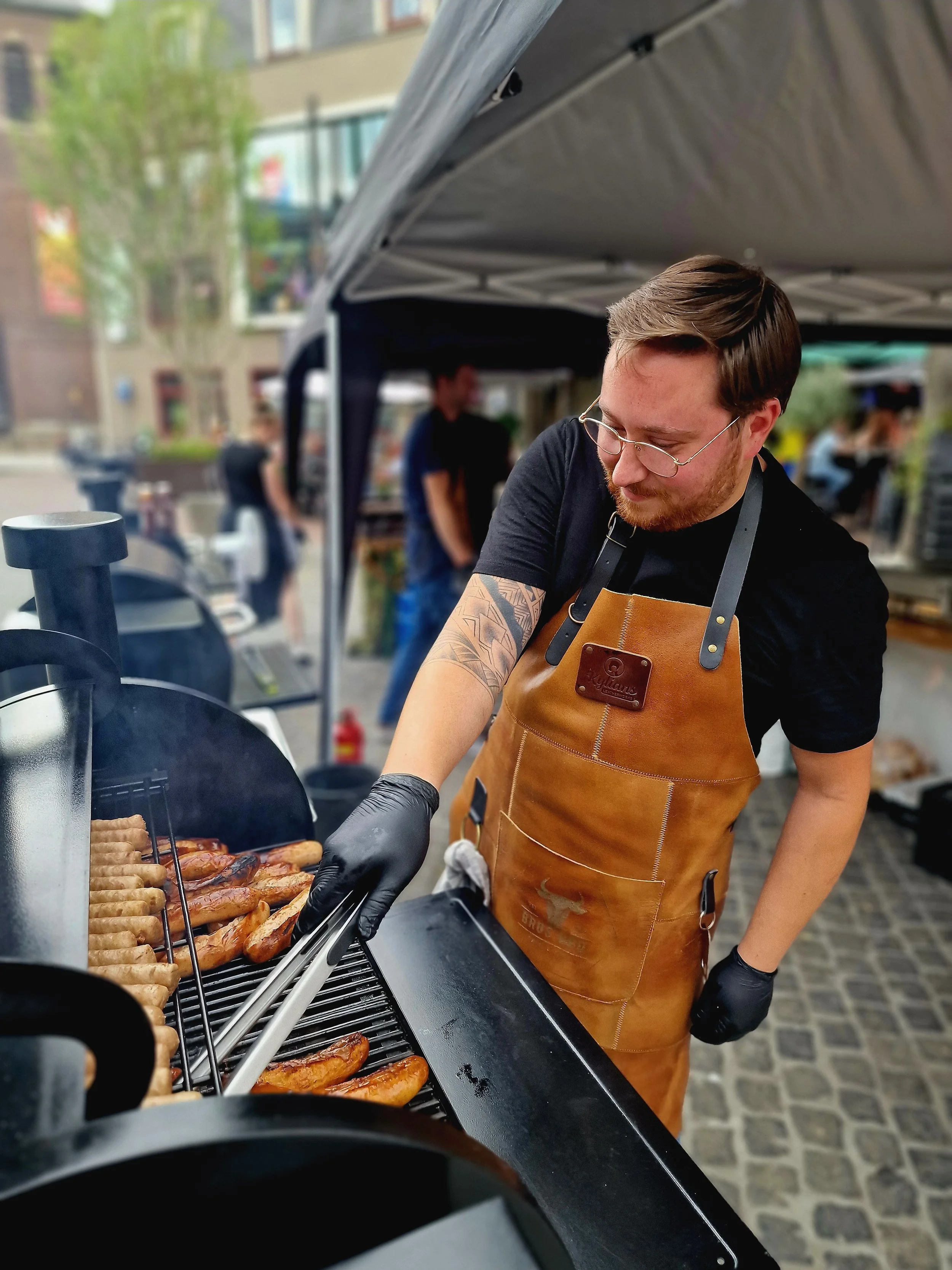 Man die hotdogs en worstjes op een barbecue grilt op een buitenmarkt.