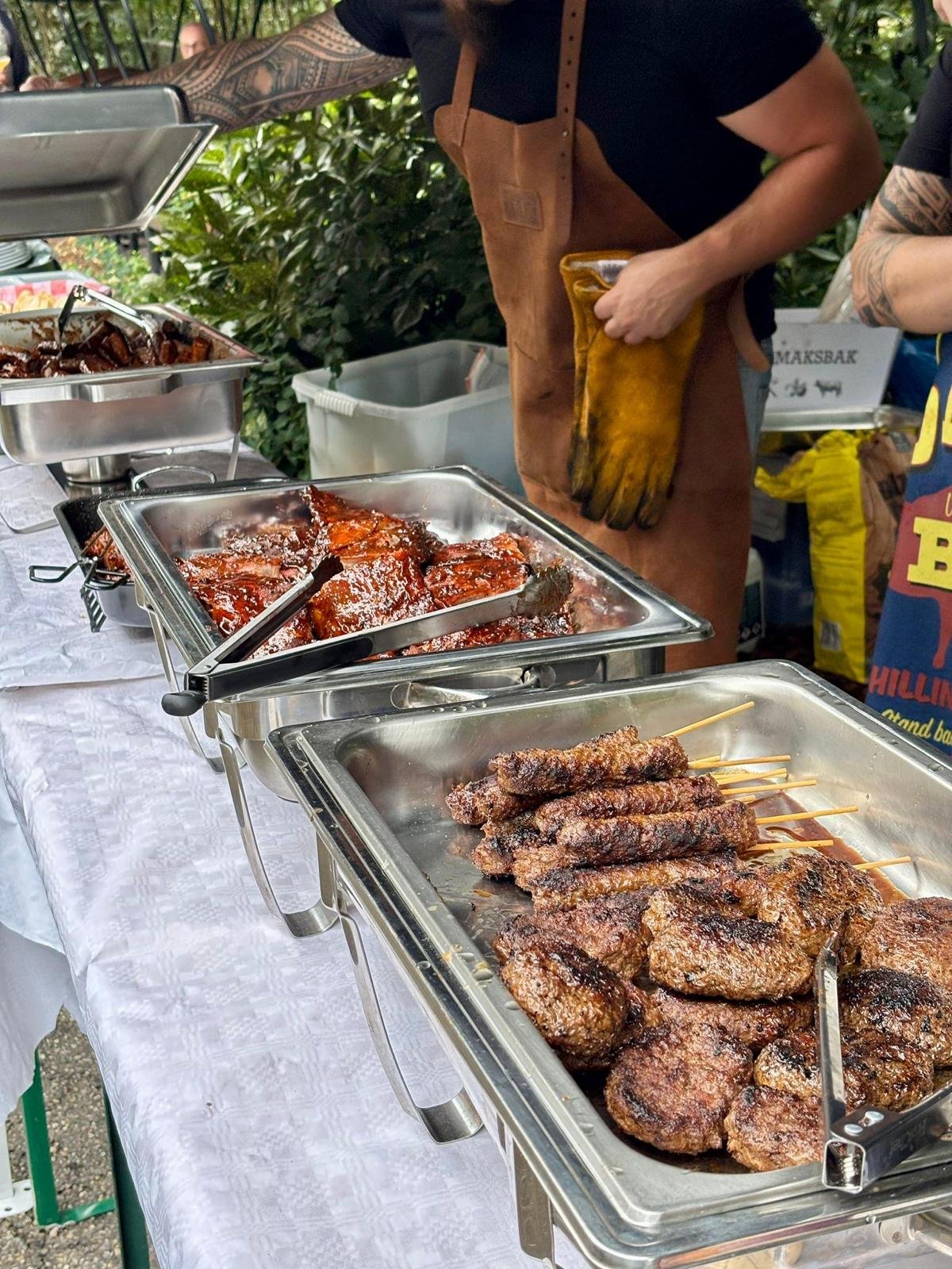 Gerechten met gegrild vlees en saté op een buffettafel, met twee mensen ernaast.