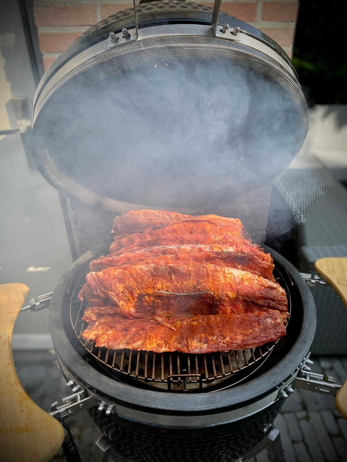Rook stijgt op uit eenketel met barbecue met op de grill een rack spareribs bedekt met barbecuesaus.