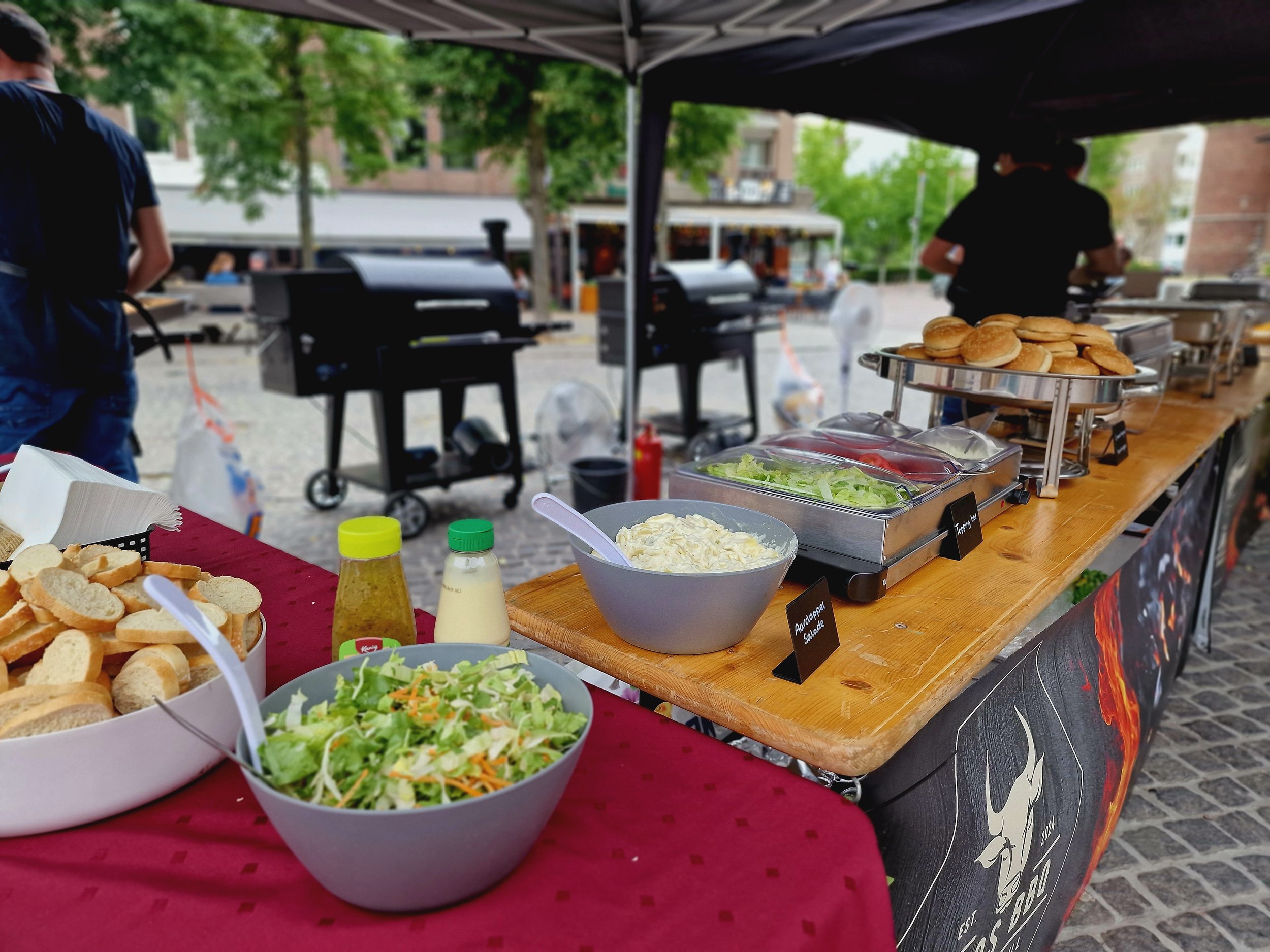 Buffet met broodjes, salade, gebakken kipstukjes en saus, klaar voor een barbecue.