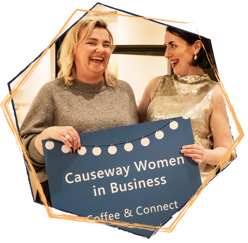 Two women smiling and holding a sign that reads 'Causeway Women in Business, Coffee & Connect', at a social event.