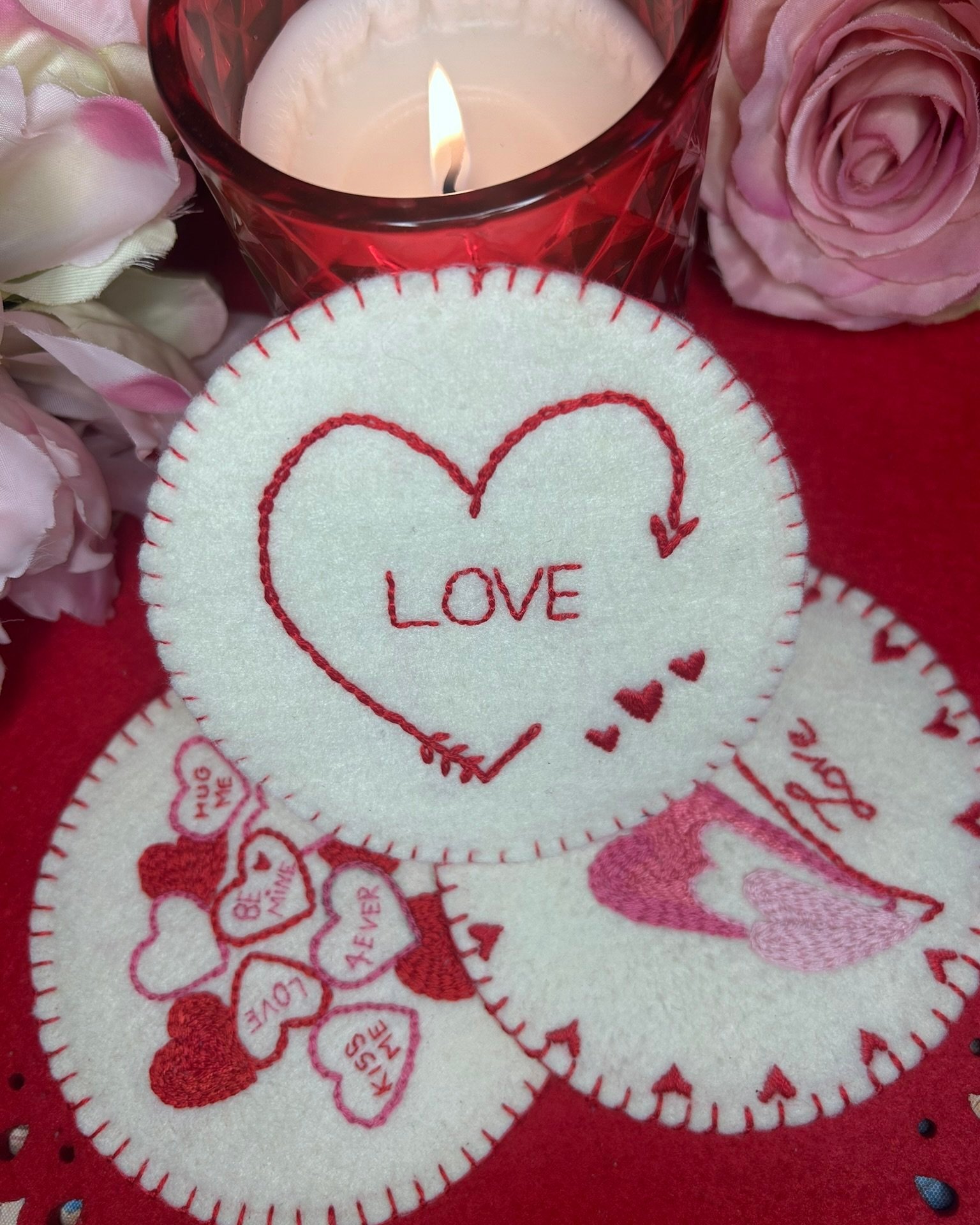 Handcrafted felt coasters with red and white designs, including hearts and the word 'LOVE,' surrounded by pink roses and a red candle.