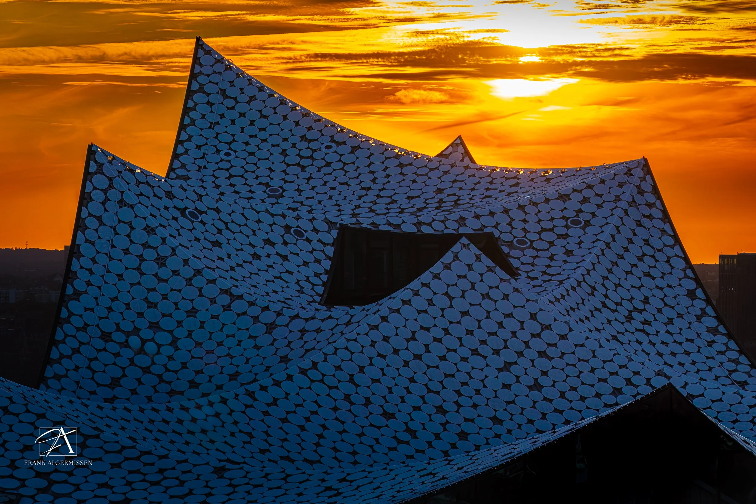 Hamburg Elbphilharmonie with a wavy roof covered in circular tiles, silhouetted against a vibrant orange sunset sky with clouds.