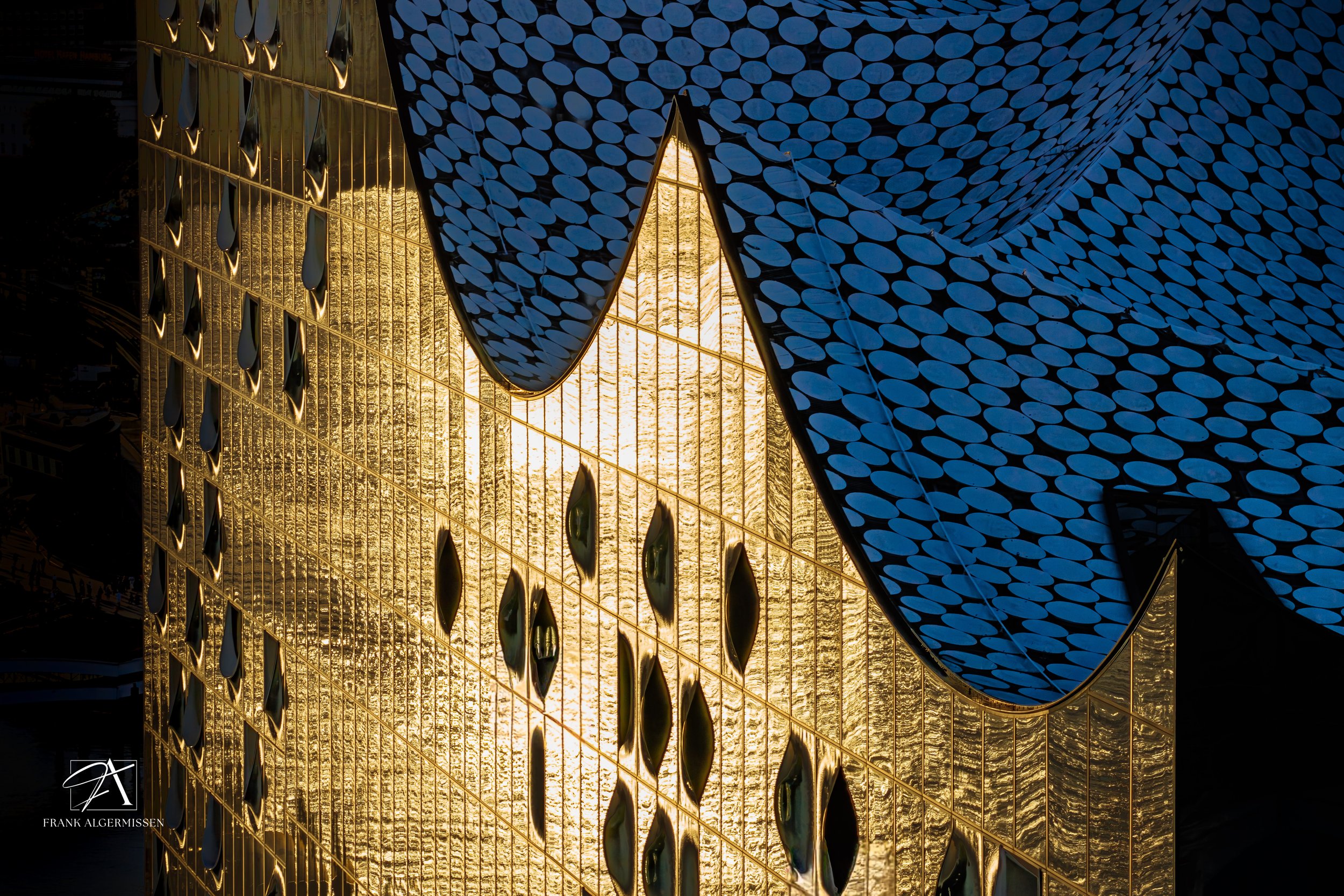 Close-up of a modern building facade with gold and blue decorative elements, reflecting sunlight.