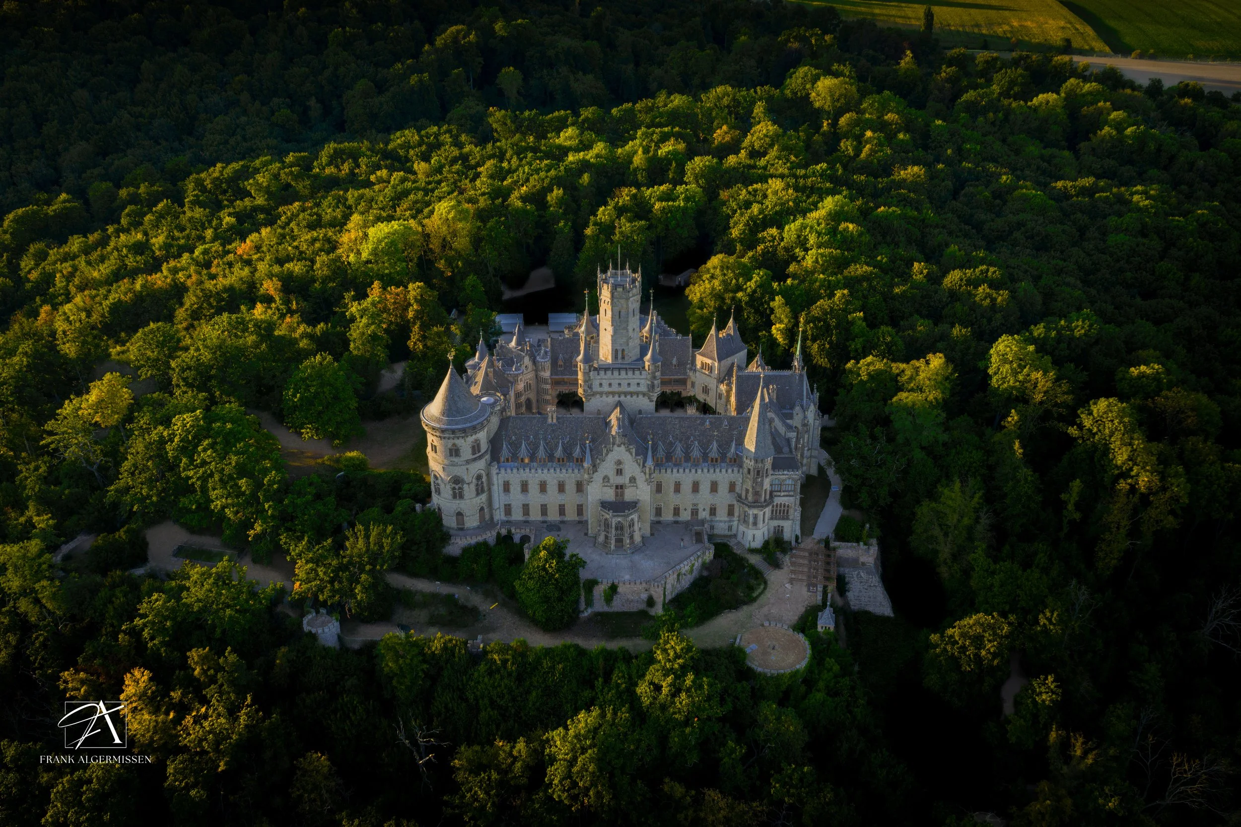 An aerial view of a large, historic castle called "Marienburg" surrounded by dense green forest.