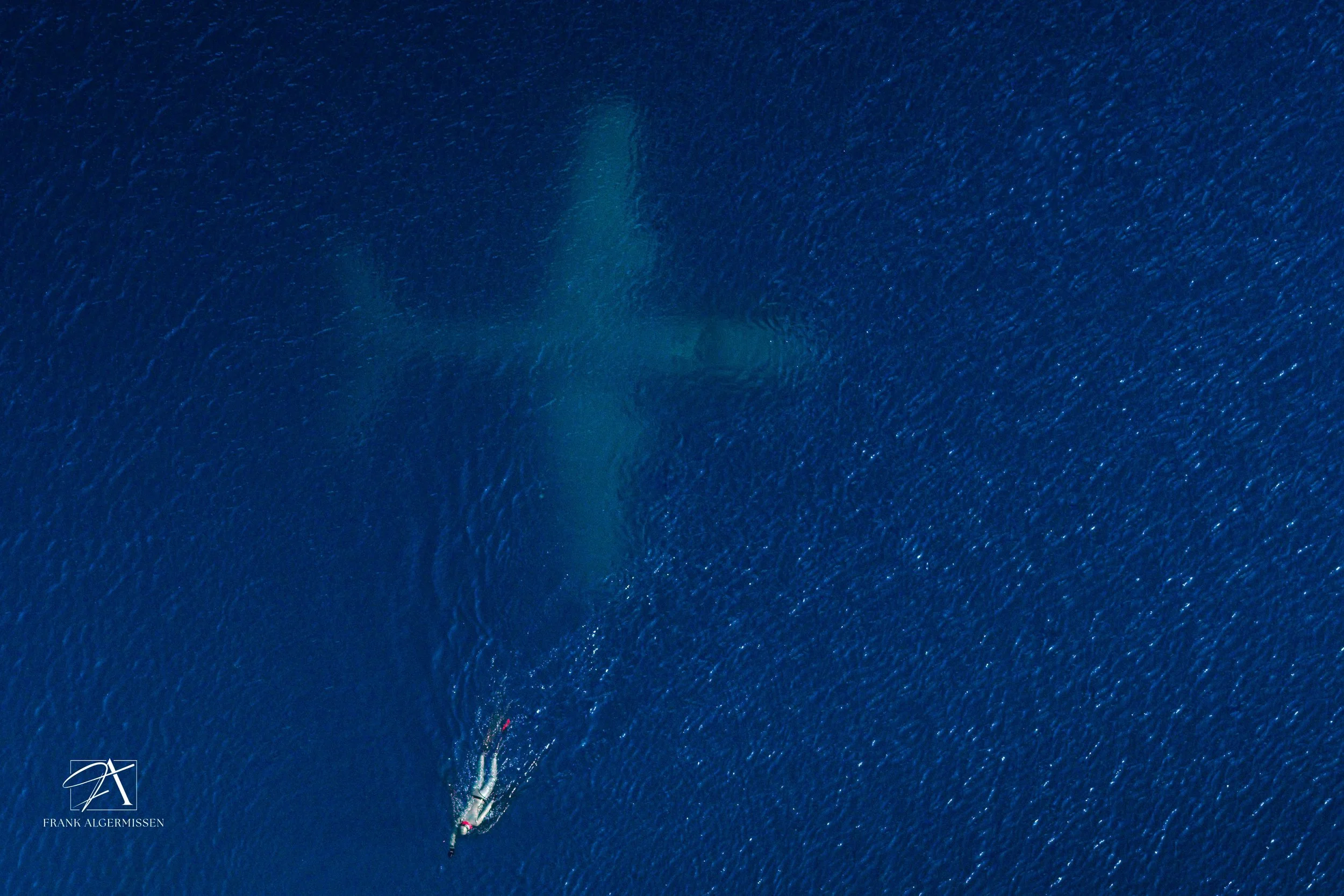 An aerial view of a boat with two people on it, sailing through the open ocean, creating a wake behind them.