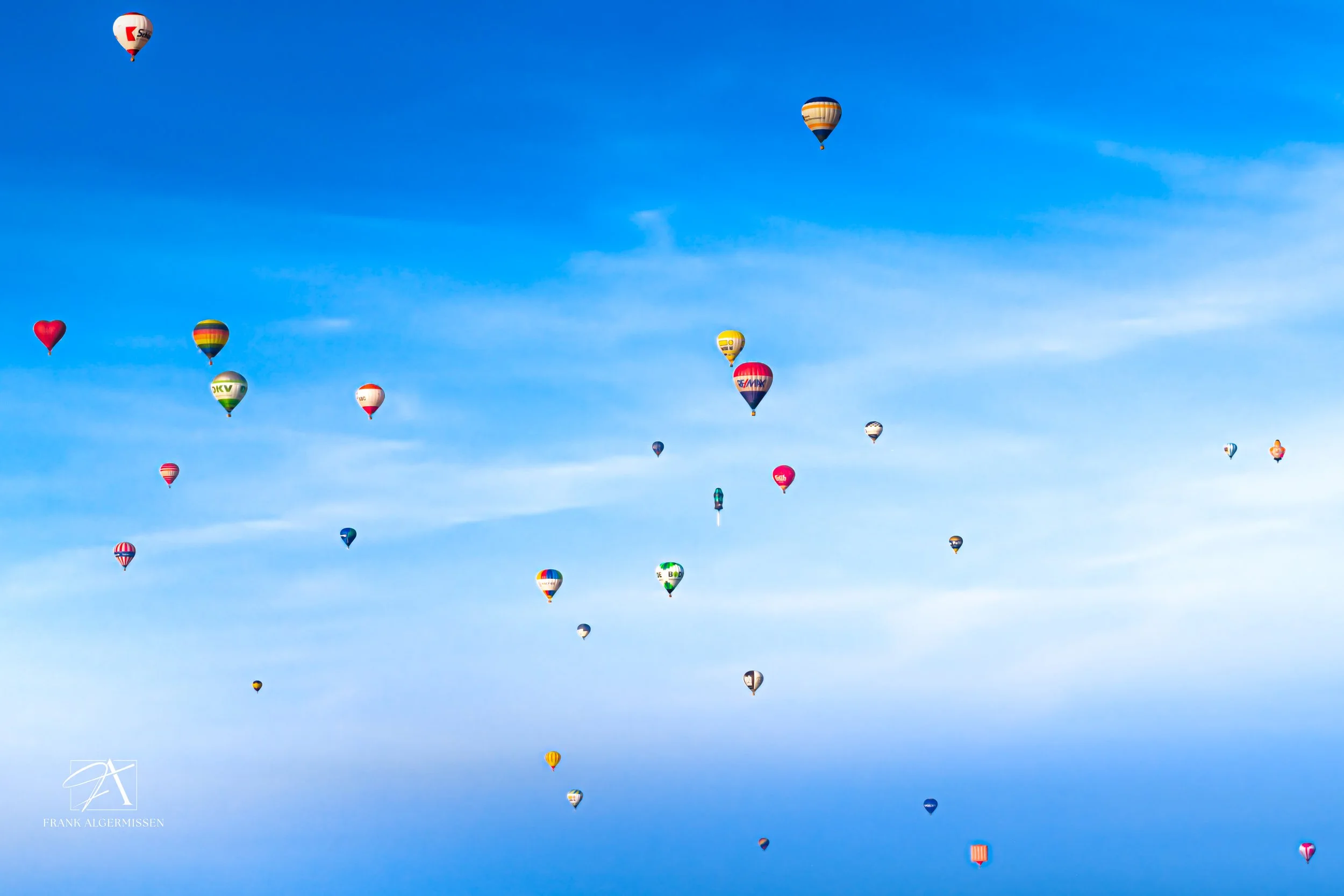 An aerial view of multiple colorful hot air balloons floating in a clear blue sky.