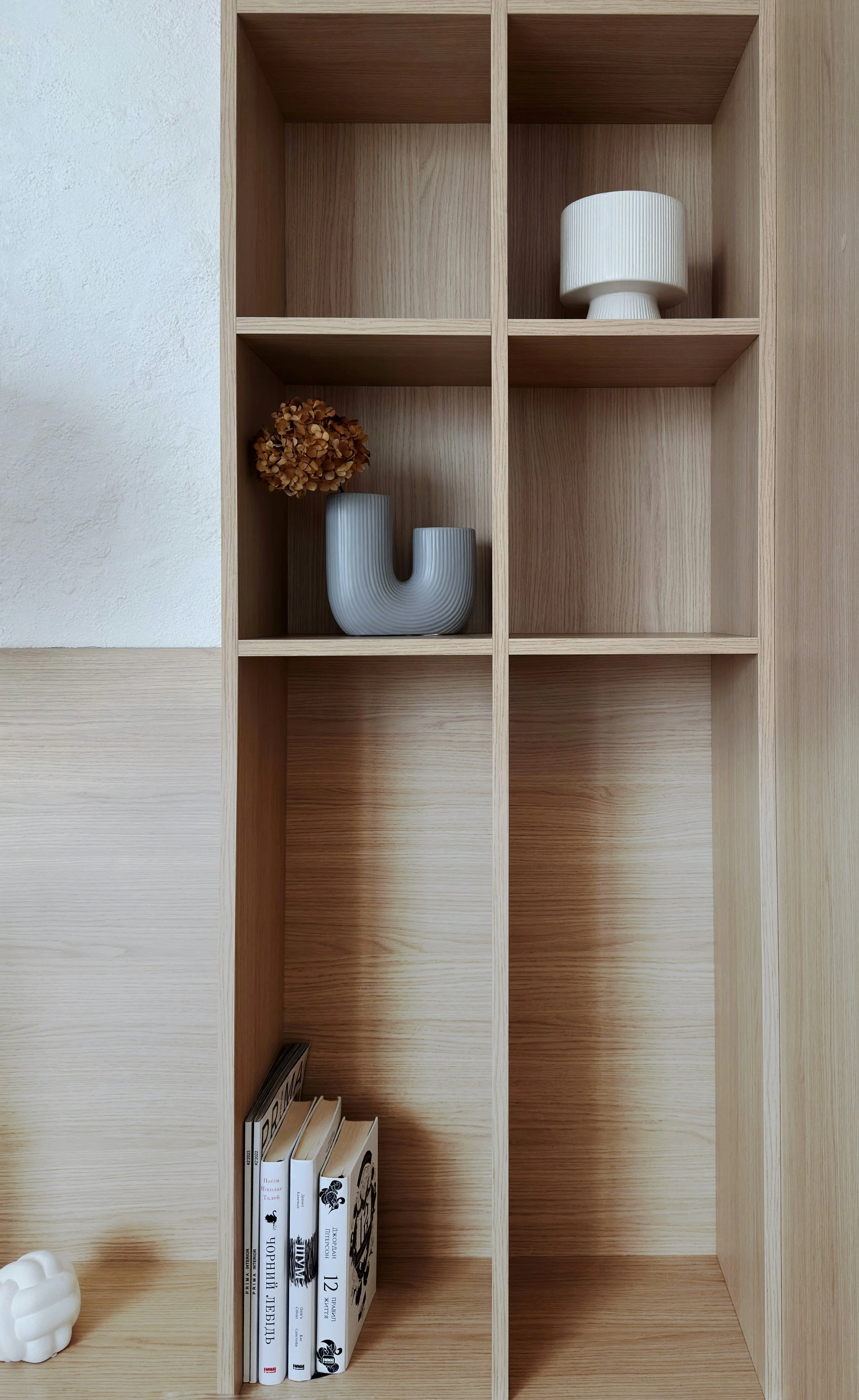 Empty wooden shelving unit with decorative vases, dried flower, and books.
