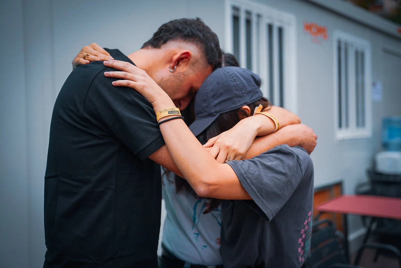Two people embracing each other tightly, faces pressed together, outdoors near a building.
