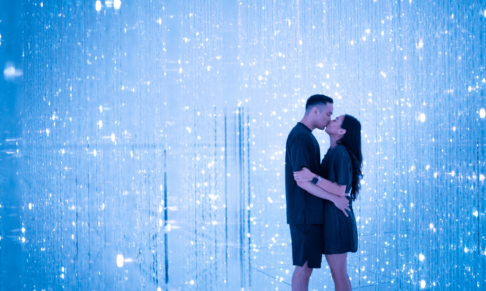 A young couple kissing in front of a digital blue LED light display.