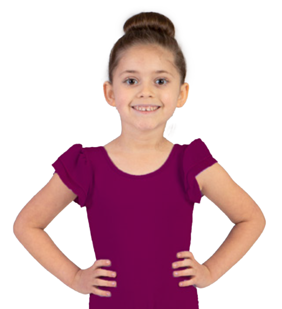 A young girl with brown hair tied in a bun, wearing a purple dress with ruffled sleeves, standing with her hands on her hips and smiling at the camera.