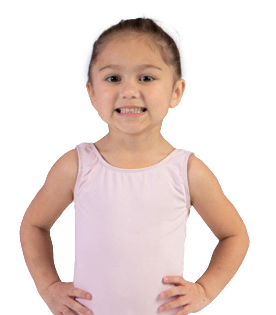 A young girl with brown hair tied back, standing with hands on her hips, smiling with a slight grimace, wearing a pink sleeveless top.