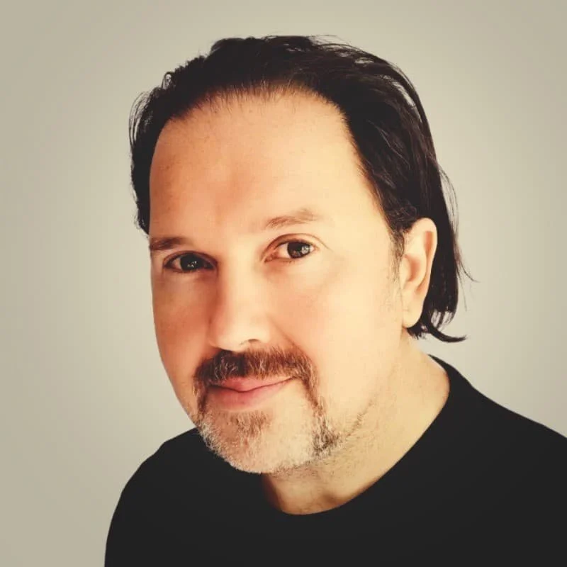 Denis hat dunkle etwas laengere Haare, ein wenig Bart und er traegt ein schwarzes Shirt