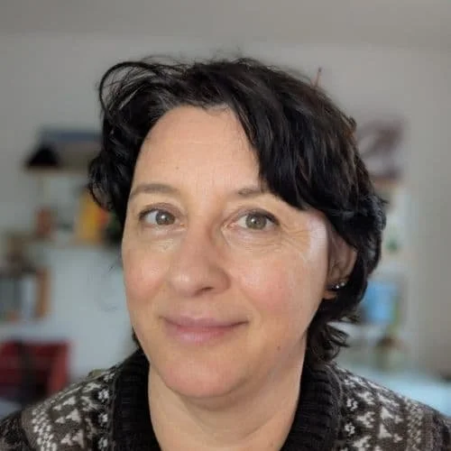 Porträt einer Frau mit kurzen dunklen Haaren, die lächelnd in die Kamera schaut, im Hintergrund eine Hausküche.