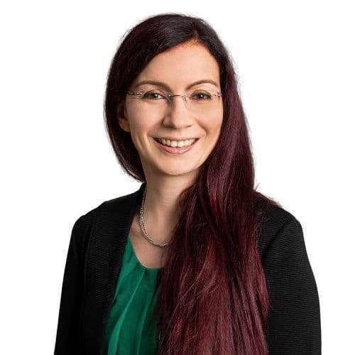 Lächelnde Frau mit Brille, dunkle Haare und grünem Oberteil, auf weißem Hintergrund