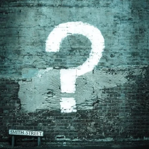 Weiße Fragezeichen-Graffito auf einer alten Ziegelmauer, unter einem Straßenschild mit der Aufschrift 'SMITH STREET'.