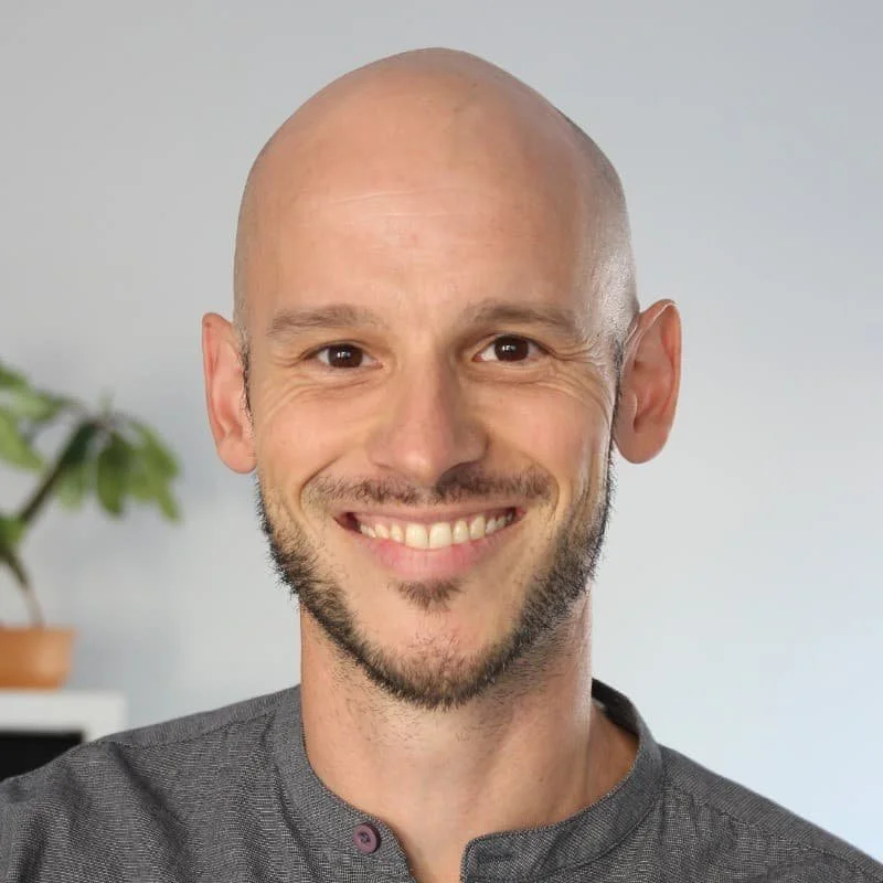 Sebastian hat einen Bart und keine Haare, er traegt ein graues Shirt.