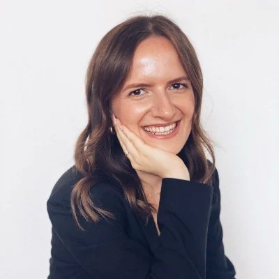 Lächelnde Frau mit braunen Haaren, trägt schwarze Bluse, vor weißem Hintergrund