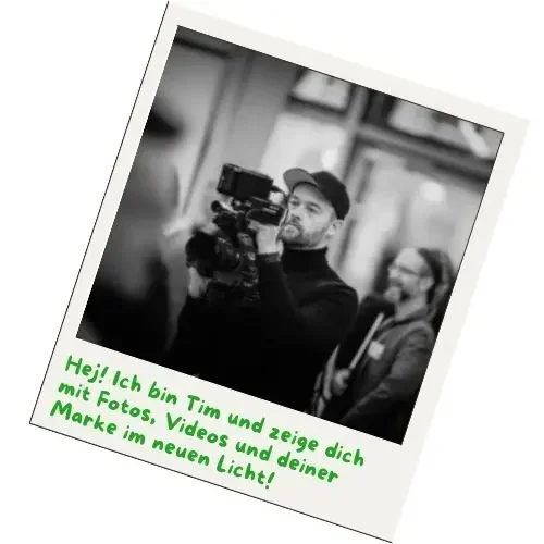 Polaroidfoto mit einem Mann, der eine Filmkamera in der Hand haelt. Er traegt ein schwarzes Basecap und einen schwarzen Rollkragenpullover. Im hintergrund sind Menschen zu sehen.