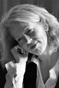 Jutta hat schulterlanges Haar, sie traegt eine weisse Bluse und eine schwarze Weste.